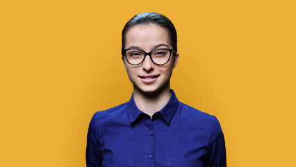 Fototapeta premium Headshot portrait of young female student looking at camera on yellow background