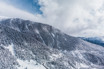 Aerial view of a mountain road in the middle of fairytale snowy mountains. Winter landscape over Vallter 2000 road. Setcases, Ripollés, Girona Pyrenees, Catalonia. Vacations, travel, winter tourism.