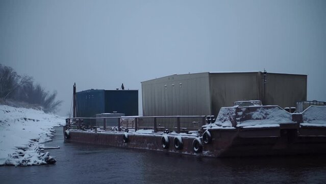 Barge with containers on river in winter. Clip. Barge transports cargo with containers along river in winter. Winter river transportation by barge