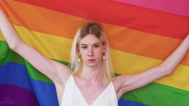 Beutiful young transgender man lifing rainbow flag from her head in the air