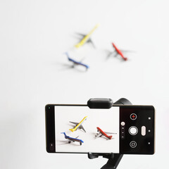 Mobile phone on gimbal and a mini tripod takes pictures of toy passenger aircraft models. Сoncept...