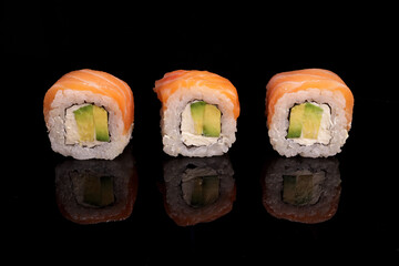 Row of sushi, rolls with salmon and avocado on a mirror black surface