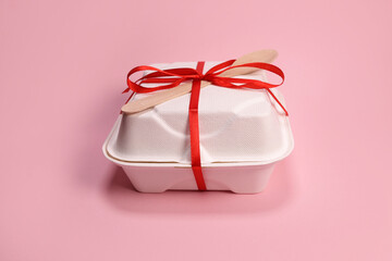 Cardboard box with bento cake tied with a ribbon with a wooden spoon on a pink background. Birthday gift