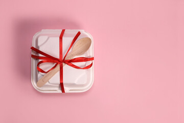 Cardboard box with bento cake tied with a ribbon with a wooden spoon on a pink background. Birthday gift