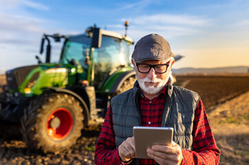 Senior farmer with tablet in field with tractor in background
