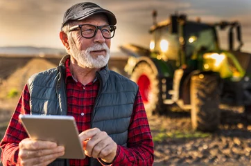 Cercles muraux Tracteur Senior farmer with tablet in field with tractor in background