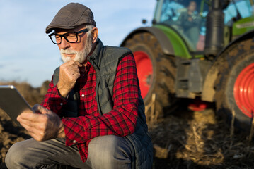 Senior farmer with tablet in field with tractor in background