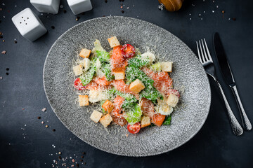 Italian food Caesar salad with salmon, parmesan cheese, lettuce, tomatoes, croutons on a dark table.