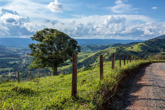 Fence and tree in the foreground with blue sky and hill in the background. Green mountains of Serra da Mantiqueira in the state of Minas Gerais, Brazil