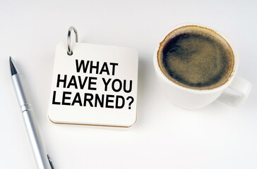 On a white surface, a cup of coffee, a pen and a notepad with the inscription - what have you learned