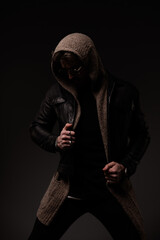 Fototapeta na wymiar mysterious man with hoodie and leather jacket posing while looking down