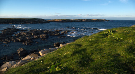 Rocky shore covered with green grass and blue sea with rocky islands