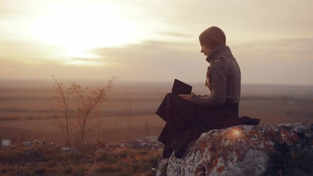 A woman reads a book at sunset. A girl reads the Bible in the open air. Female holding bible in hands and studying word of God at sunrise on top of mountain. Finding Truth in the Scriptures. High qual