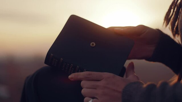 Close-up. A woman opens a Bible, flips through the pages. A girl reads the Bible in the open air, studies the word of God at sunset on top of a mountain. Finding Truth in the Scriptures. High quality 