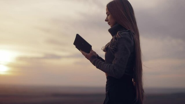 The woman closes the Bible, prays. A girl reads the Bible in the open air, studies the word of God at sunset on top of a mountain. Finding Truth in the Scriptures. High quality 4k footage