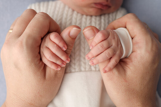 The newborn baby has a firm grip on the parent's finger after birth. Close-up little hand of child and palm of mother and father. Parenting, childcare and healthcare concept. Professional macro photo.