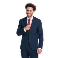portrait of happy businessman with curly hair adjusting tie and smiling