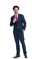 happy young man in elegant suit smiling, holding hand in pocket and fixing suit