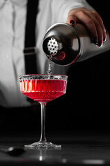 the bartender makes a kir royal cocktail in a  crystal glass on a dark background