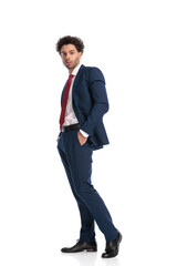 side view of elegant businessman with curly hair posing with hands in pockets