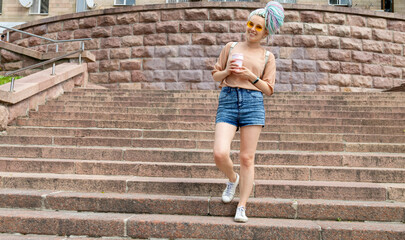 Young girl is walking up the stairs with a cup of coffee. Modern woman with yellow glasses and...
