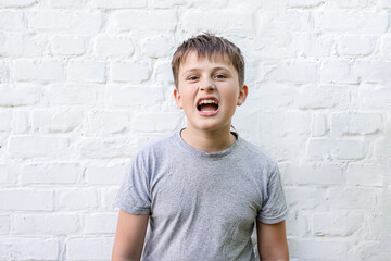 The teenager screams in shock. Portrait of a boy with an open mouth against a white brick wall.