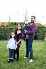 Fototapeta premium The interracial family is active and enjoys a day at the park. Successful adoption. The family poses standing as they look into the camera. Concept of multiethnic or interracial family.