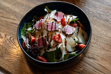 Close-up view of tuna salad with pieces of medium-rare grilled with sesame tuna, cheese, strawberry and fresh vegetable on a bowl. Soft focus. Top table view. Food background theme.