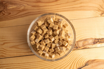 Several cubes of brown sugar in a glass bowl, close-up, on a wooden table, top view.