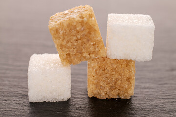 Several cubes of white and brown sugar, close-up, on a slate serving board.