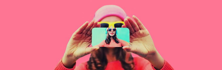 Close up of modern young woman stretching her hands taking selfie with smartphone on pink background