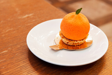 A cake in the shape of a tangerine lays on a white saucer, close up