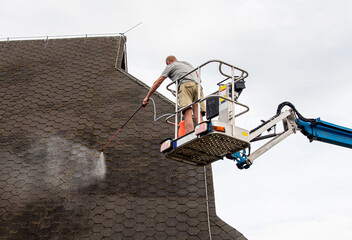 Man a homeowner spraying moss removing chemical to a domestic home roof in summer outdoors. Moss...