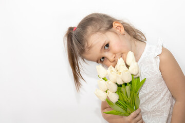 Obraz na płótnie Canvas Portrait of a little blonde girl with a bouquet of spring flowers on a light background. child in white dress holding a bouquet of tulips in her hands. space for text. spring concept