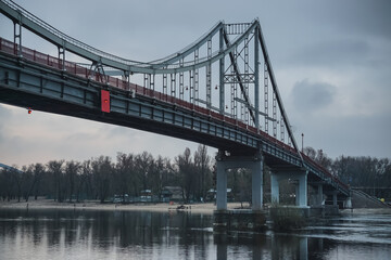 Obraz na płótnie Canvas Pedestrian bridge with a bike path across the Dnieper River in the center of Kyiv, on a cloudy spring day