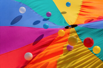 Multicolor-patterned kids play parachute with colorful bouncing balls. Rainbow colors toys for...