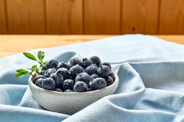 Fresh organic blueberries. Juicy ripe bilberry in white bowl on wooden table. Antioxidant and healthy eating concept.
