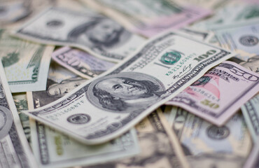 One hundred dollars close-up in large quantities lie on the table. Scattered money lies in the background all over the surface. Blurred background on a hundred dollar bill.