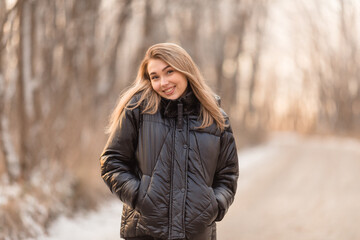 Young girl in black clothers walks in the winter forest. Sunset and snow