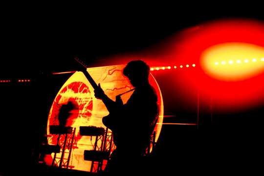 Silhouette of a guitarist performing energetically under striking red stage lights, enhancing the fiery and passionate atmosphere of the live music scene.