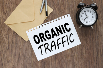 wooden background. sheet of paper and table clock. text in black font .ORGANIC TRAFFIC. Business concept