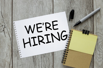 we are hiring. wooden background. sheet of paper and yellow sticker .text in black font