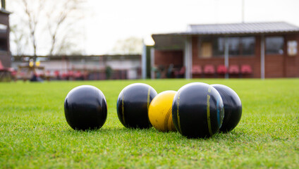 Crown green bowling balls gathered round the yellow Jack during bowling competition outdoors, a...
