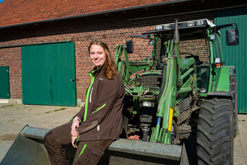 Junge Landwirtin steht in einer Frontladerschaufel auf ihren Hof.