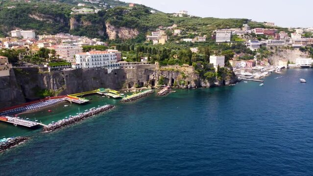 Aerial drone footage of Bagni Salvatore at steep cliff coastline of Sorrento town, Campania, Italy. Summer beach resort platforms on Sorrentine peninsula with people sunbathing on lounger from above.