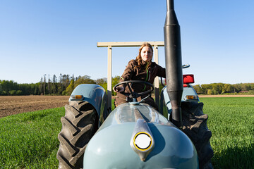 Junge Frau mit Spass an der Landwirtschaft sitzt auf einem Oldtimer - Traktor mitten im Getreidefeld bei Sonnenschein. © Countrypixel