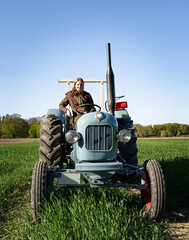 Junge Frau mit Spass an der Landwirtschaft sitzt auf einem Oldtimer - Traktor mitten im Getreidefeld bei Sonnenschein. © Countrypixel