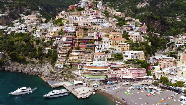 Aerial drone footage of Marina Grande beach, chiesa (church) Santa Maria Assunta in Positano, Amalfi coast, Campania, Italy. Parasol, sun loungers, people swimming, colourful cliff villas from above.