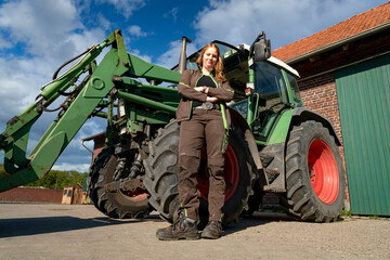 Junge Landwirtin steht vor ihrem Trecker auf den elterlichen Hof.