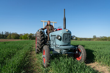 Junge Frau mit Spass an der Landwirtschaft sitzt auf einem Oldtimer - Traktor mitten im...